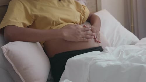 Pregnant Woman Applies Cream to Stomach in Bedroom