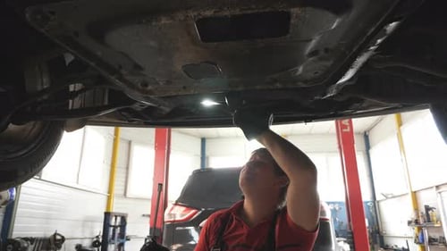 Auto Mechanic Inspecting Bottom of a Car During Maintenance at Service