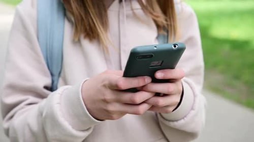 Little Schoolgirl Typing Message On A Phone On Park