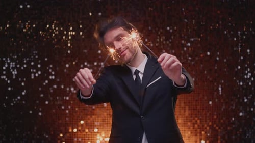 Smiling Man in Suit Holds Sparklers Against Gold Backdrop