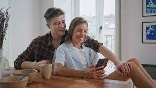 Smiling Couple Looking at Mobile Phone in Home
