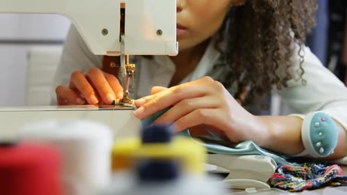 Front view of African American female fashion designer working with sewing machine in workshop 4k