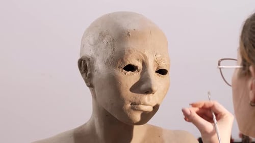 Female Sculptor Adding Clay On The Undereye Of Sculpture And Polish With A Carving Tool At Workshop.