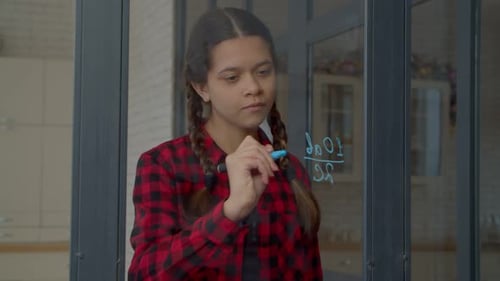Écolière adolescente intelligente résolvant un exemple mathématique sur une vitre