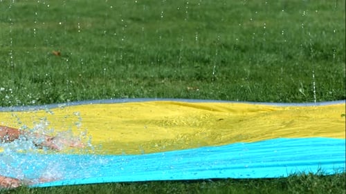 Boy Slides on Backyard Water Slide on Lawn