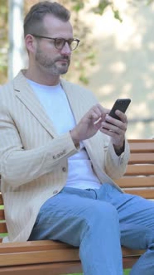 Man Sitting on Bench Using Mobile Phone Outside