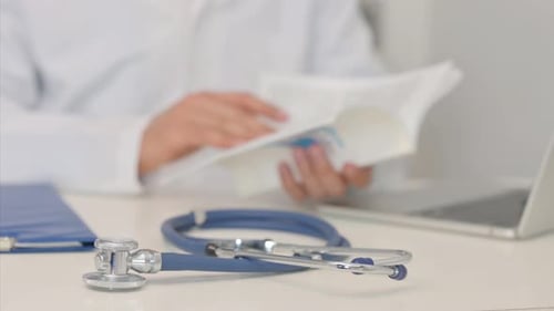 Stethoscope on Desk with Blurred Doctor Reading