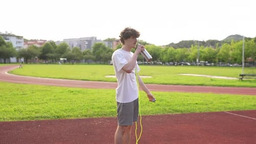 Man Drinking Water Before Jumping Rope in Park
