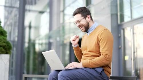 Happy excited businessman received great news on laptop while sitting on a bench on the street near