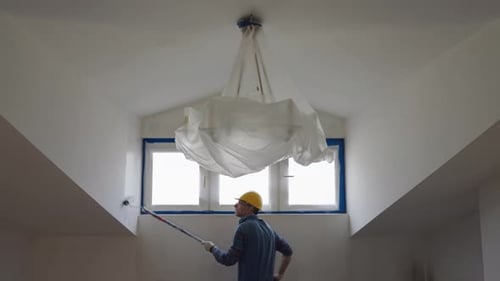 Ein Mann malt eine Wand mit einer Rolle und repariert den Raum im Dachgeschoss