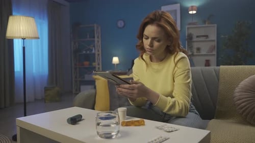 A Woman with a Vial of Pills Sits on a Sofa in the Living Room A Woman Reads the Name of a Medicine