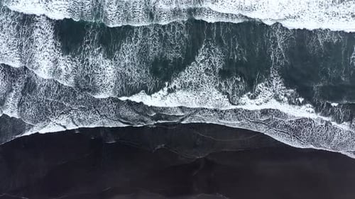 Slow motion aerial view of waves rushing to the shore on black volcanic sand. Atlantic Ocean, Icela