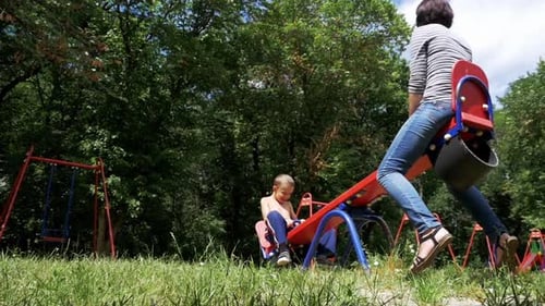 Happy Child Boy and His Mother Swinging on a Street Counterweight Swing at Playground in Slow Motion