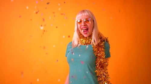 smiling party with confetti at a celebration, blonde caucasian girl in studio on yellow background
