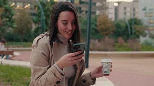 Woman Using Smartphone in Urban Park with Coffee