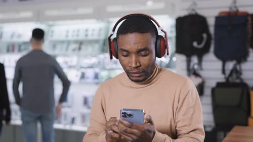 An African Man in an Eleutronics Store Chooses Wireless Headphones for Himself