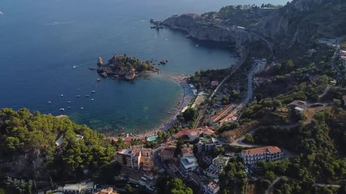 Aerial super wide drone shot of the coast of Taormina in Sicily, Isola Bella, with soft sunset light