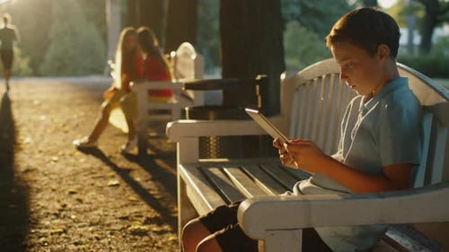 Boy is Sitting at Park and Using Tablet PC at Sunset Time