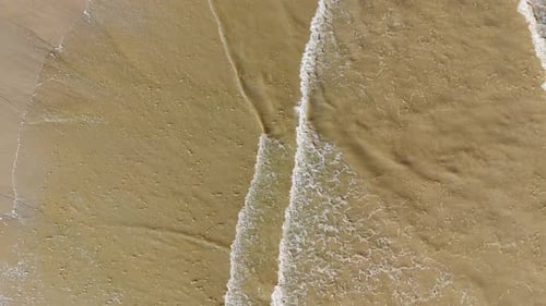 Aerial footage of waves gently breaking on the beach, with golden sand.