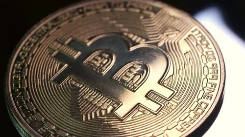 Pièce cryptographique 4K en monnaie Bitcoin tournant lentement dans le sens des aiguilles d'une montre avec une lumière réfléchissante sur fond noir
