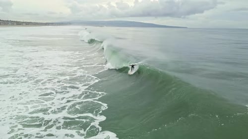 Un surfeur solitaire surfe habilement sur une vague massive et perd l'équilibre en atteignant la plage