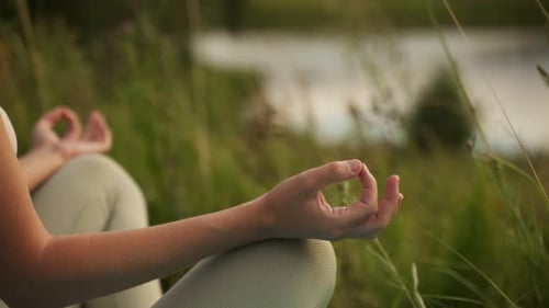 Closeup of the Hands of a Caucasian Woman Meditating in the Lotus Position in Nature By the Pond