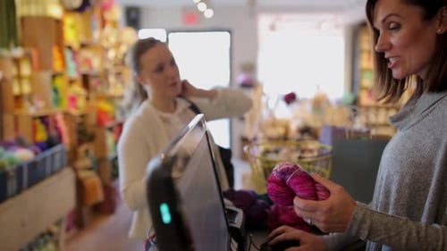 Woman buys wool at yarn store counter with assistance from entrepreneur