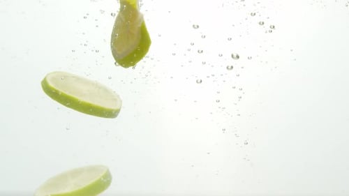 Green citrus fruit slices dropped into water isolated on white background