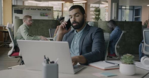 Man Talking on Phone While Using Laptop in Office