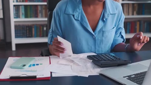 Close Up Woman Hands Using Calculator and Checks Sits at Table with Laptop