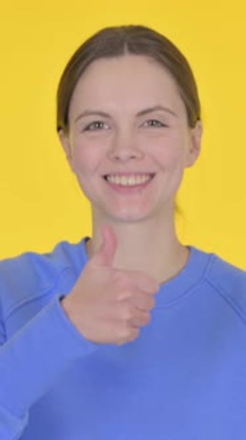 Smiling Woman Gives Thumbs Up on Yellow Background