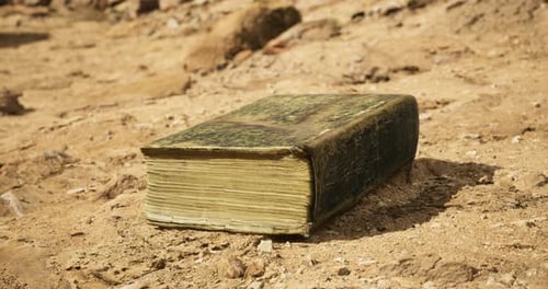 Ancient Book Rests on Sandy Ground at Historical Site During Daylight