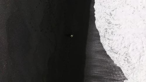 Man Walking Black Sand Beach with White Tide