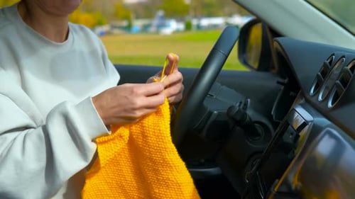 Woman knitting bright yellow yarn inside parked car