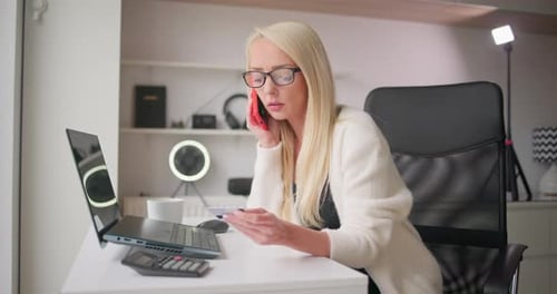 Woman Talking on Phone, Holding Credit Card at Desk