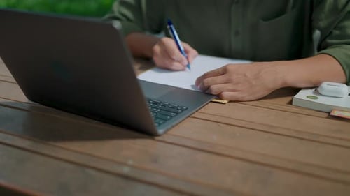 Nahaufnahme der Handschrift eines asiatischen Mannes auf einem Dokument, der ernsthaft arbeitet und sich Notizen im Freien macht i