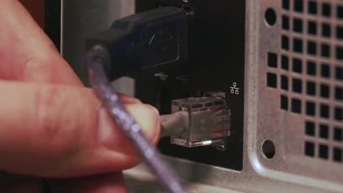 Nahaufnahme einer männlichen Hand, die ein Netzwerkkabel in eine Computerbuchse einsteckt. Das Patchkabel ist angeschlossen