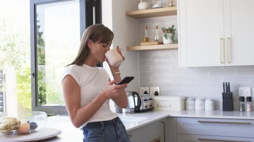 Woman Using Smartphone and Drinking Coffee at Home