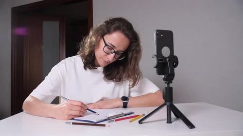 Woman Drawing at a Table in Front of Phone