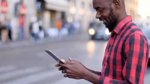 Young Black man standing in the street and using digital tablet