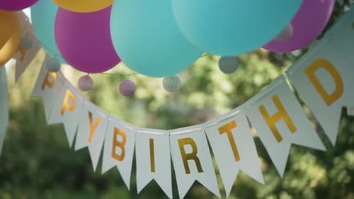 Closeup Multicolored Balloons and Happy Birthday Decoration Hanging in Sunshine in Summer Park