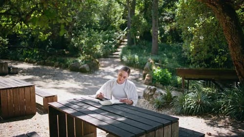 Young Woman Journaling at a Sunny Park Table