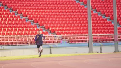 Slow motion wide shot of sport man athlete prosthesis legs is jogging on track in the stadium