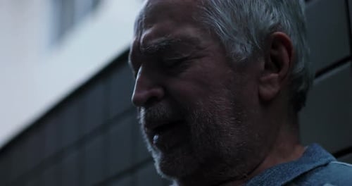 Elderly man close up with eyes closed leaning against wall expressing deep emotional struggle inner