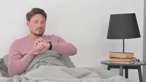 Man Using Smartwatch While Sitting Up in Bed