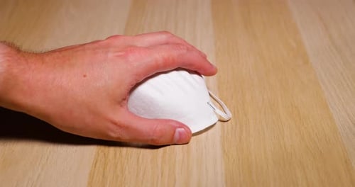 Men's hands dropping white protective mask on face and nose from wooden table on which lies protecti