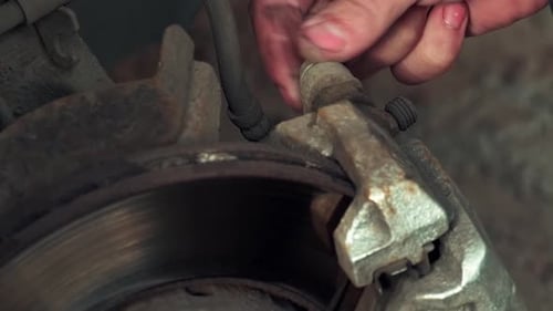 a Mechanic in a Car Repair Shop Unscrewing a Caliper Bolt to Replace Brake Pads