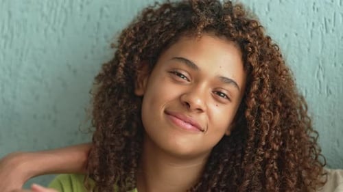 Teenage Girl With Curly Hair Leaning With Soft Smile And Calm Eyes, Close Up Showing Relaxed