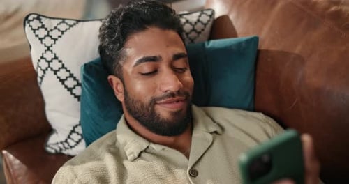 Smiling Man Relaxing on Couch with Mobile Phone