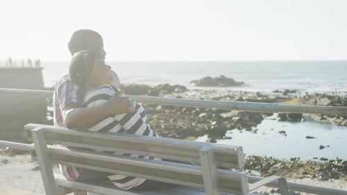 Happy senior african american couple sitting on bench on promenade by the sea, slow motion